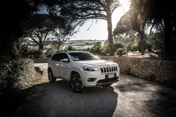 Vista lateral del Jeep Cherokee estacionado bajo árboles, resaltando su diseño robusto.