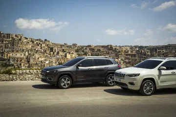 Dos Jeep Cherokee mostrando perfil lateral contra un paisaje urbano