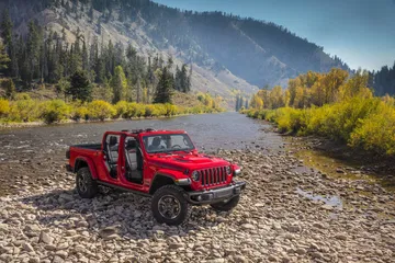 Jeep Gladiator rojo luciendo su diseño lateral robusto en paisaje montañoso.