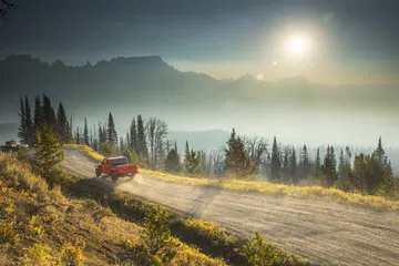 Un Jeep Gladiator rojo circulando por un paisaje montañoso al atardecer.