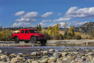 Vista lateral de un Jeep Gladiator rojo cruzando un río. Capacidad todoterreno en acción.