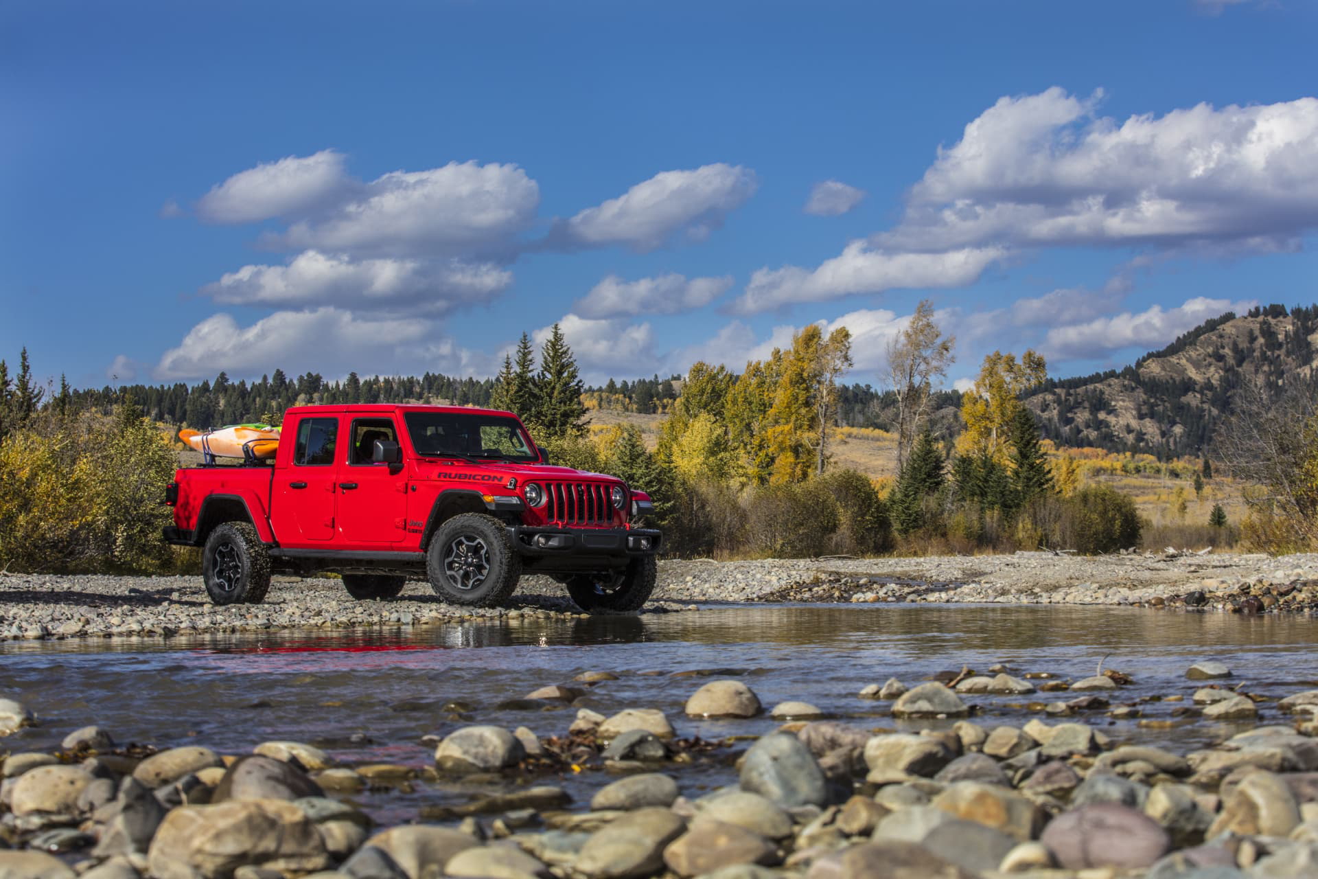 Vista lateral de un Jeep Gladiator rojo cruzando un río. Capacidad todoterreno en acción.