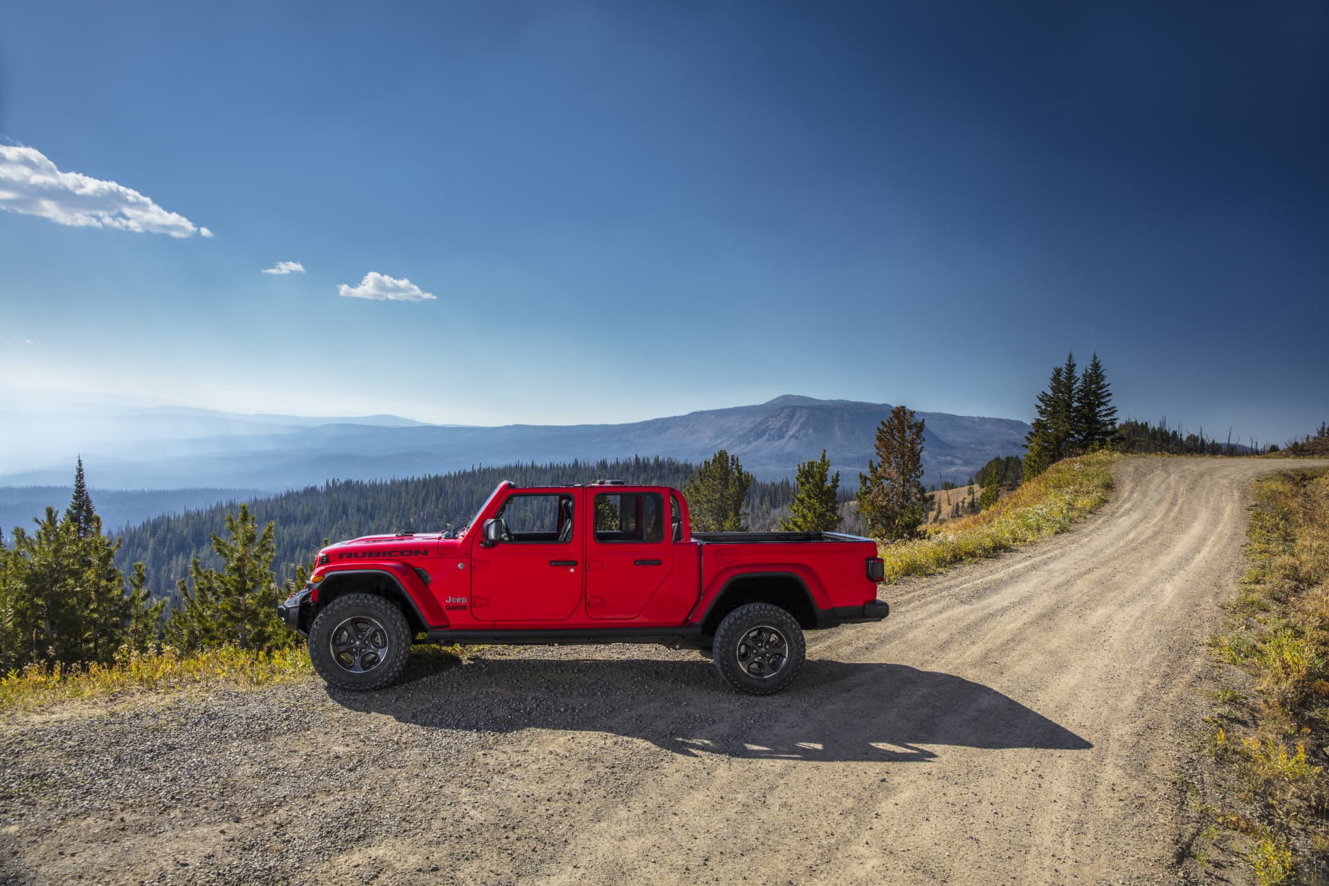 Vista lateral del Jeep Gladiator sobre una pista de tierra con paisaje montañoso.