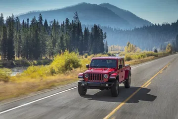 Jeep Gladiator avanzando por carretera con paisaje forestal al fondo