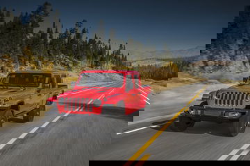 Vista lateral del Jeep Gladiator en color rojo circulando por carretera con paisaje montañoso.