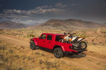 Jeep Gladiator rojo equipado para el transporte de motocicletas en terreno desértico.