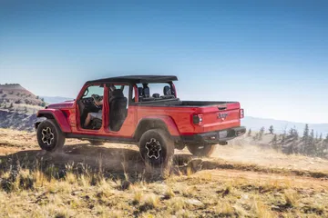 Vista lateral de un Jeep Gladiator rojo superando terreno montañoso