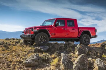 Vista lateral de un Jeep Gladiator rojo en un terreno rocoso.