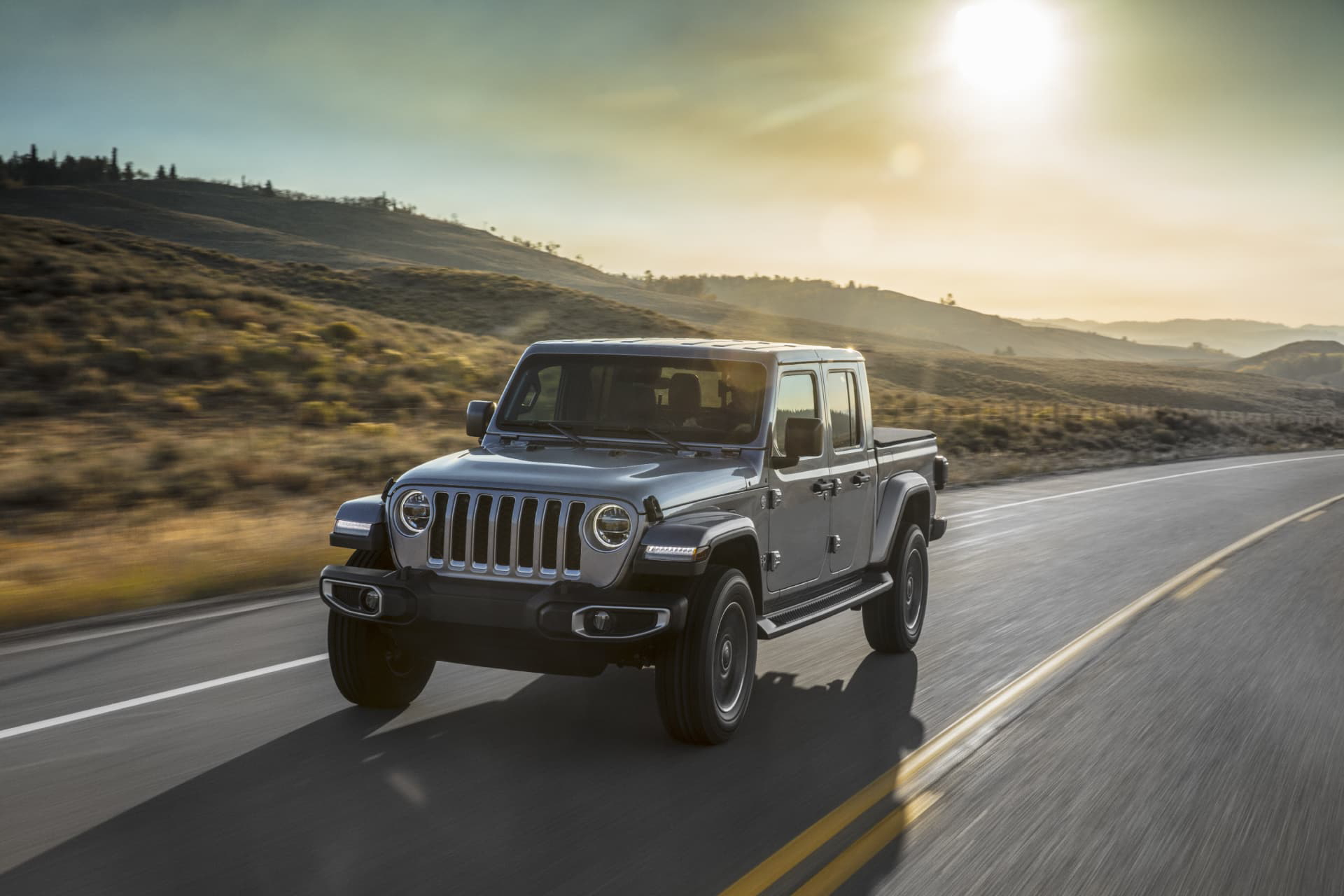 Jeep Gladiator avanzando por carretera al atardecer, vista lateral.