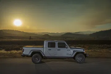 Jeep Gladiator avanzando por terreno abierto al atardecer, mostrando su imponente diseño lateral.