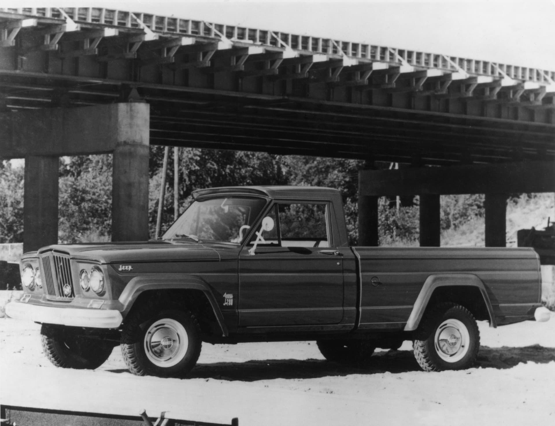 Clásico Jeep Gladiator en vista lateral bajo un puente ferroviario.
