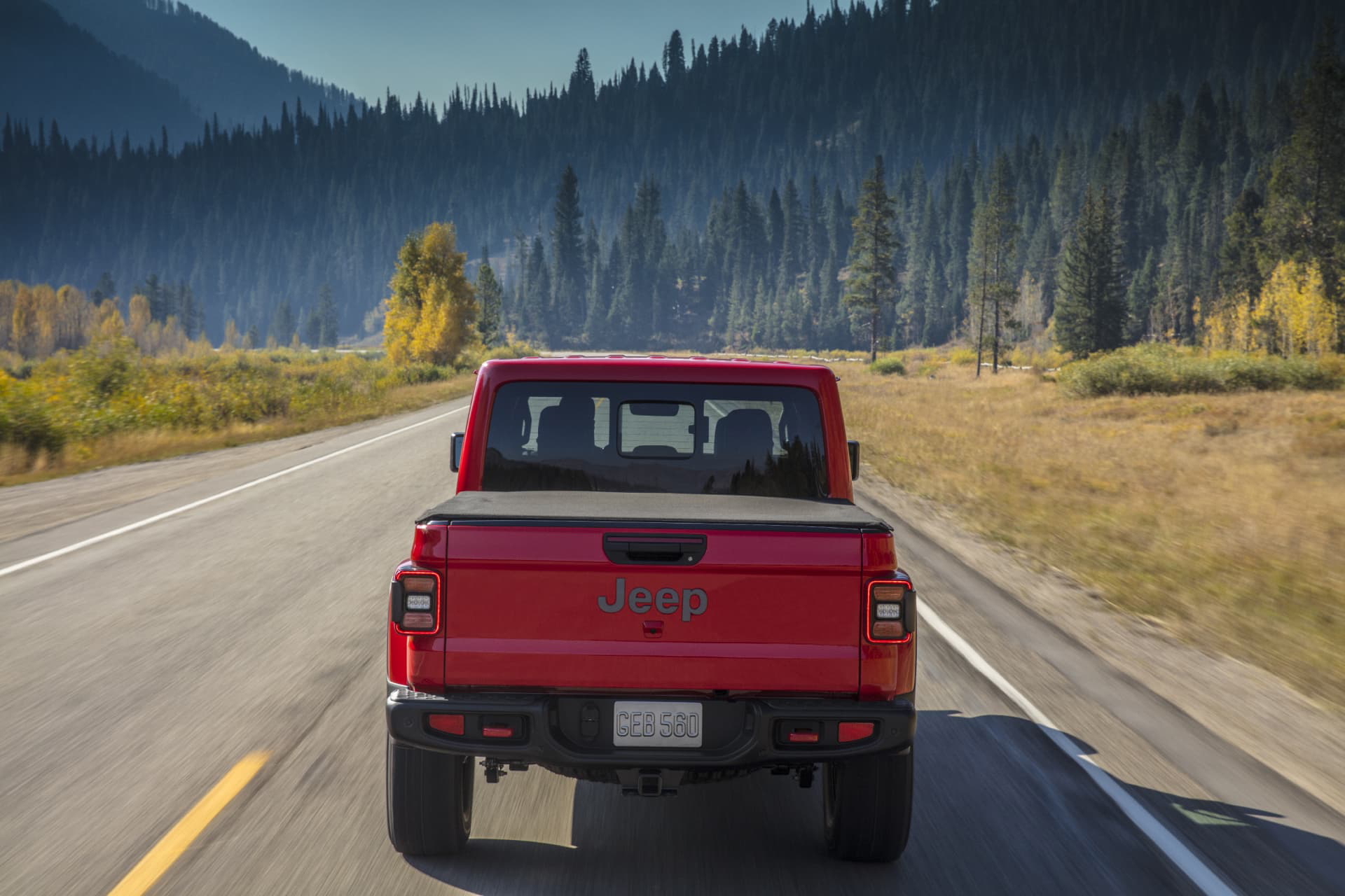 Vista trasera del Jeep Gladiator rodando por carretera con paisaje boscoso.