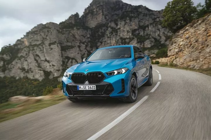 Vista dinámica del BMW X6 azul en carretera de montaña, resaltando su robustez y diseño.