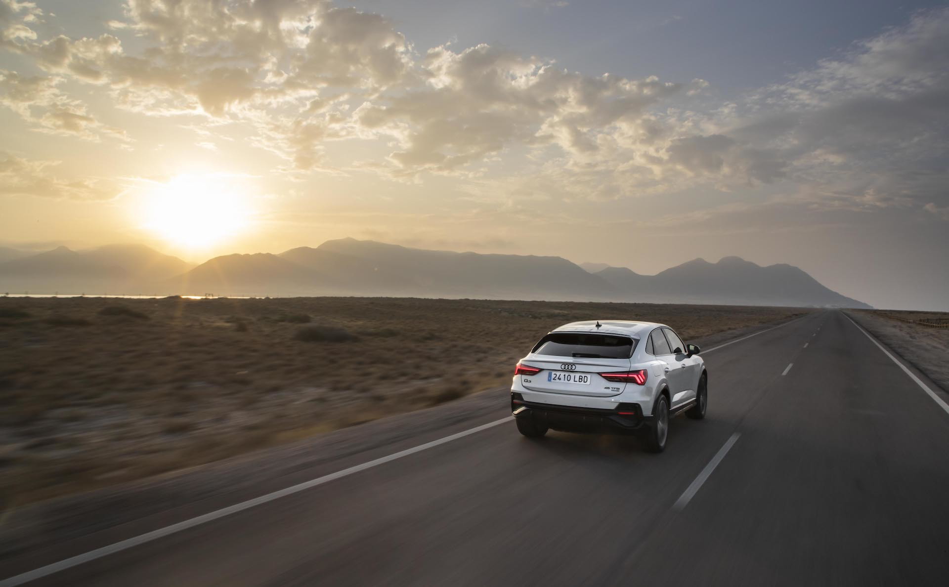 Vista dinámica del Audi Q3 Sportback recorriendo una carretera desértica al atardecer