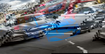 Ford Mustang Mach-E en movimiento en un entorno urbano, destacando su diseño frontal y lateral.