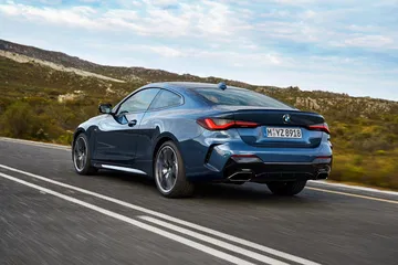 Vista dinámica del BMW Serie 4 en carretera, mostrando su diseño trasero y lateral.