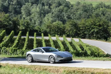 Vista lateral del Ferrari Roma en movimiento, capturado en carretera rural.