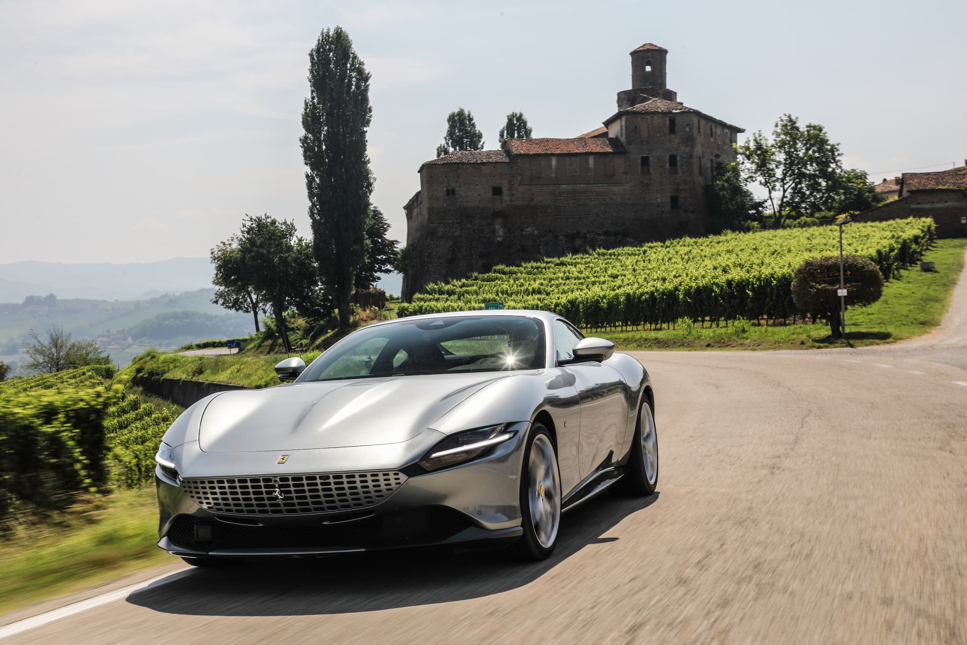 Ferrari Roma avanzando con un fondo de viñedos y una construcción histórica.