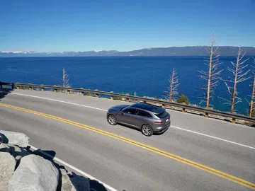 Vista lateral del Jaguar F-PACE en movimiento con vista panorámica al lago.