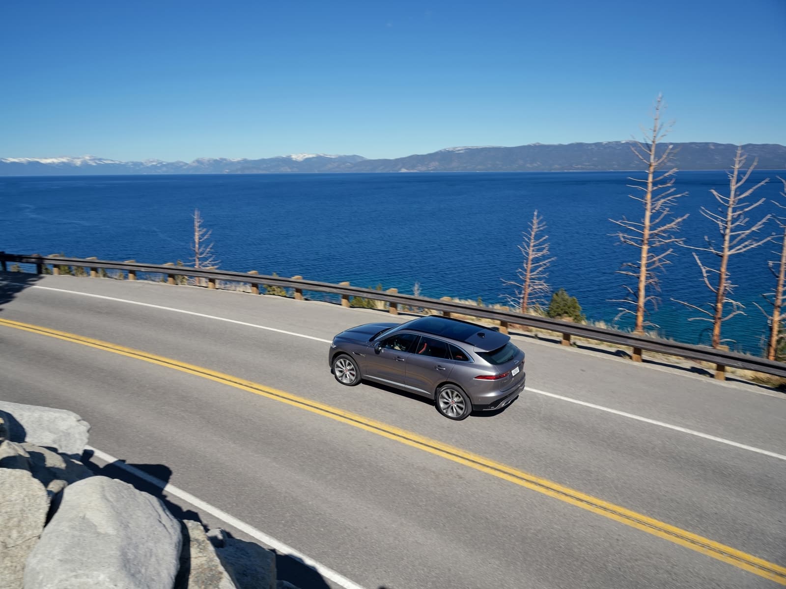 Vista lateral del Jaguar F-PACE en movimiento con vista panorámica al lago.