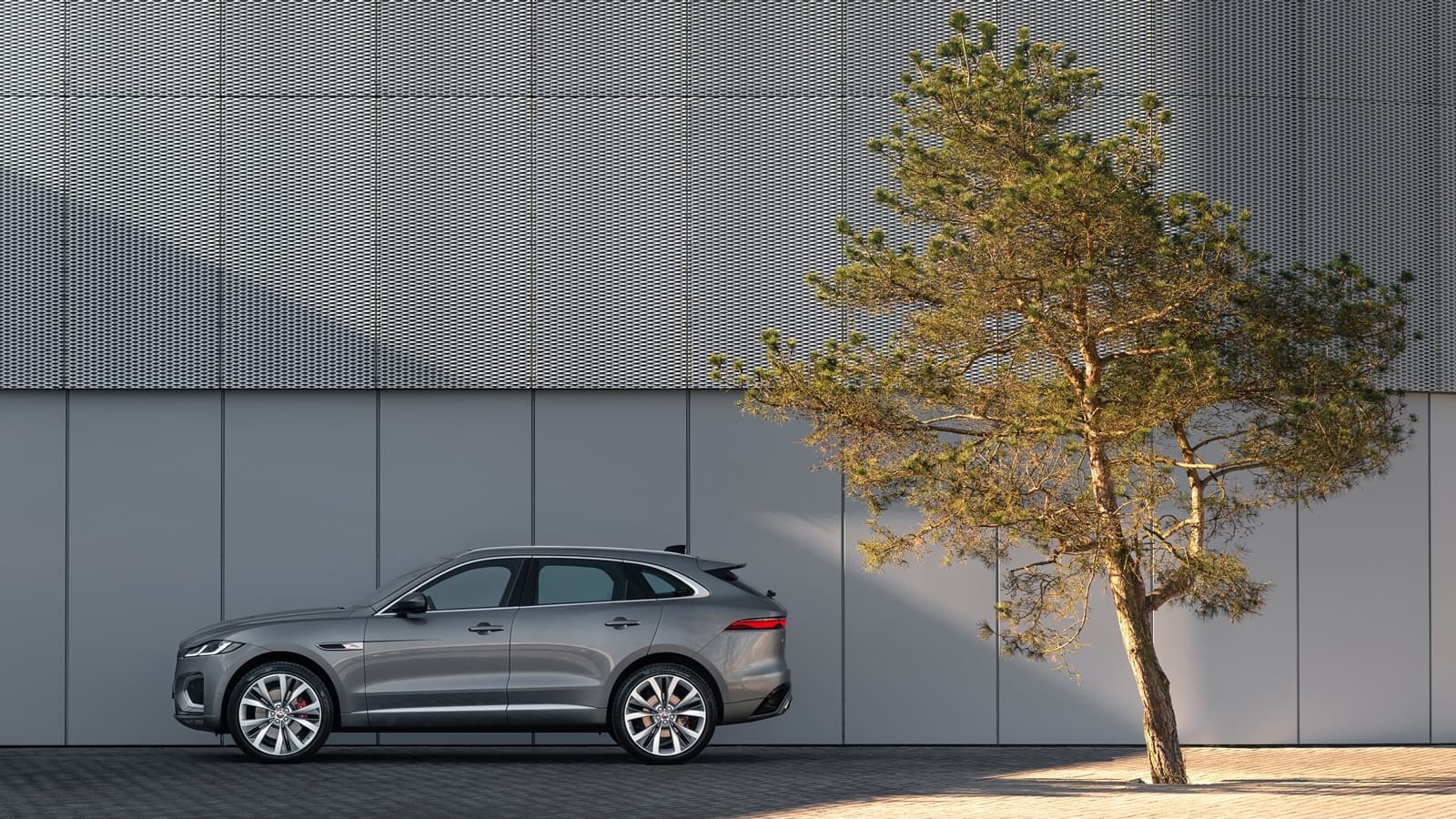Vista lateral del Jaguar F-PACE aparcado frente a una pared moderna con un árbol al lado.