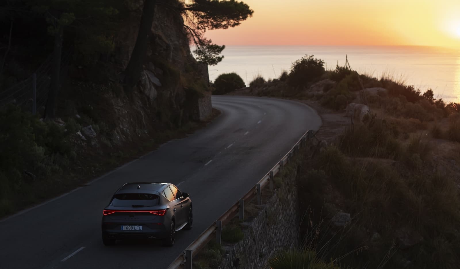 Vista trasera lateral del CUPRA León disfrutando de una carretera al atardecer.
