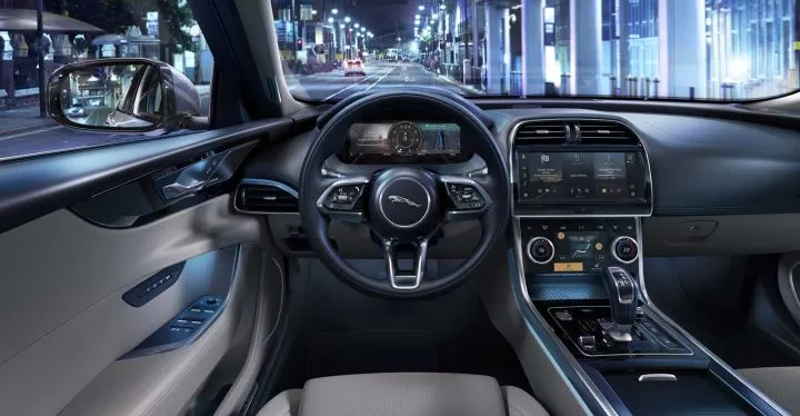Vista del volante y consola central del Jaguar XE iluminados por la noche.