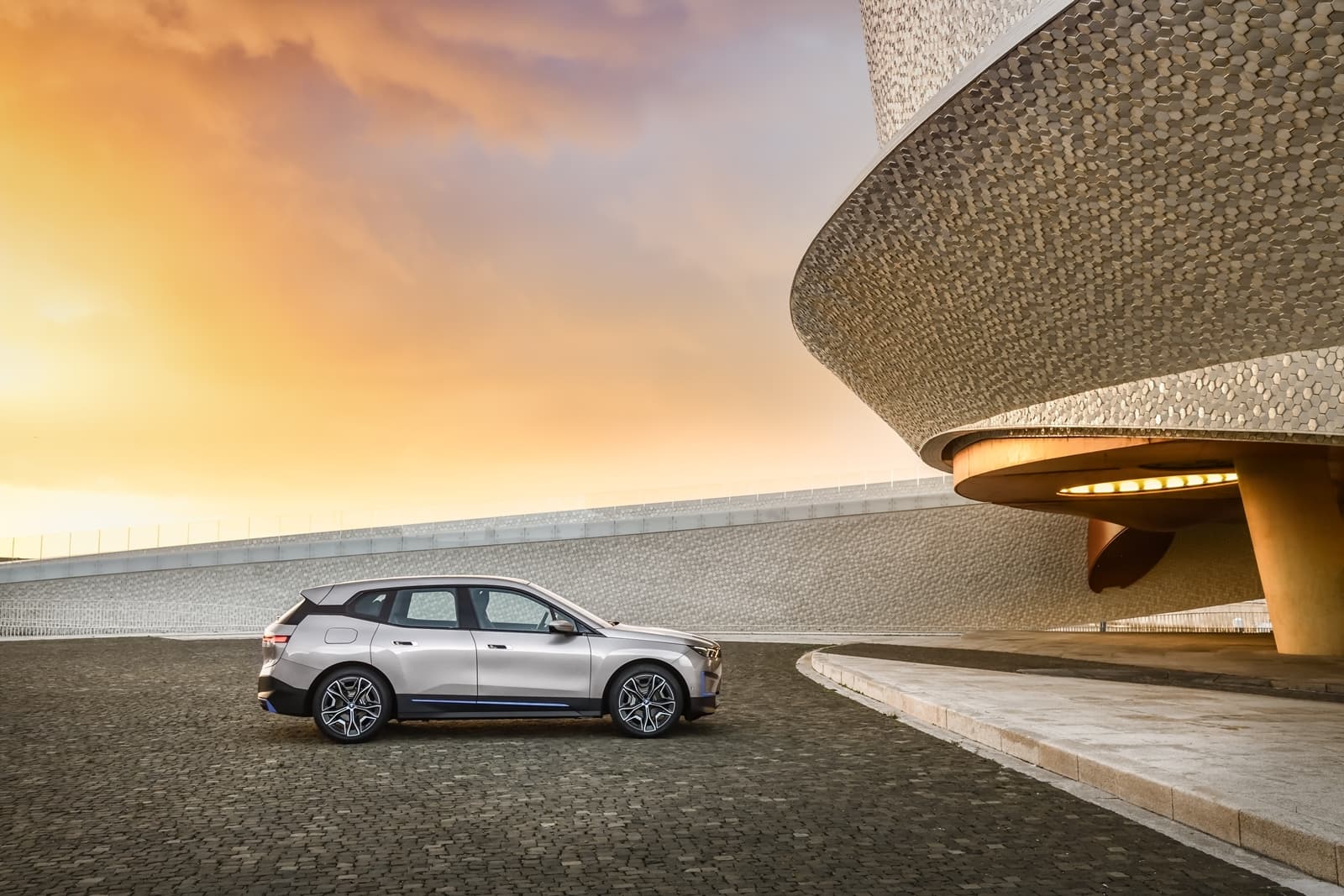 BMW iX apreciado en su lateral junto a arquitectura contemporánea.