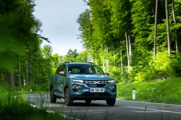 Vista angular delantera del Dacia Spring en un camino boscoso