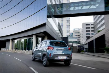 Vista dinámica del Dacia Spring en un entorno urbano, destacando su diseño frontal y lateral.