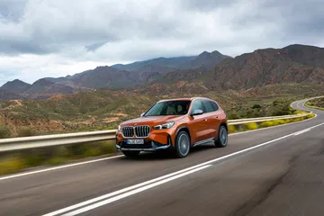 Vista dinámica del BMW X1 conduciendo por una carretera con montañas al fondo.