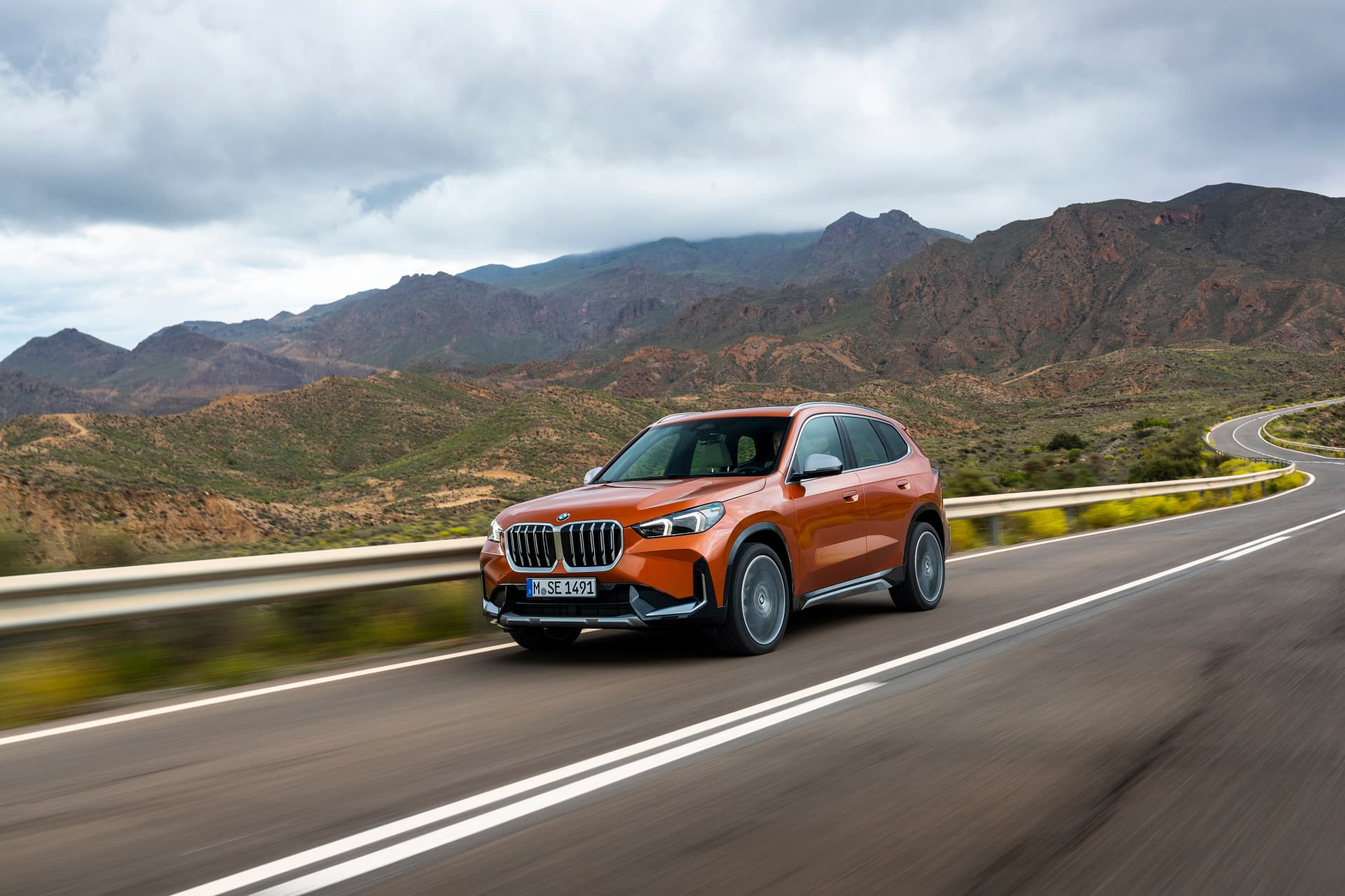 Vista dinámica del BMW X1 conduciendo por una carretera con montañas al fondo.