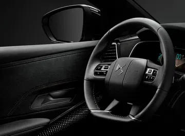 Volante de cuero con controles integrados y logo DS visible, acabados de calidad.