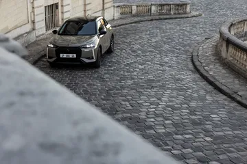 Imagen del DS 3 en movimiento por una calle adoquinada, ángulo frontal y lateral.