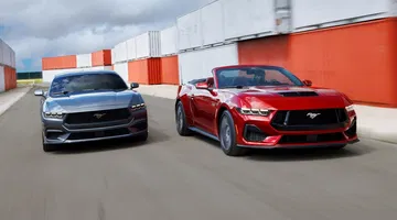 Dos Ford Mustang en paralelo, uno rojo y otro gris, ambos con diseño lateral imponente.