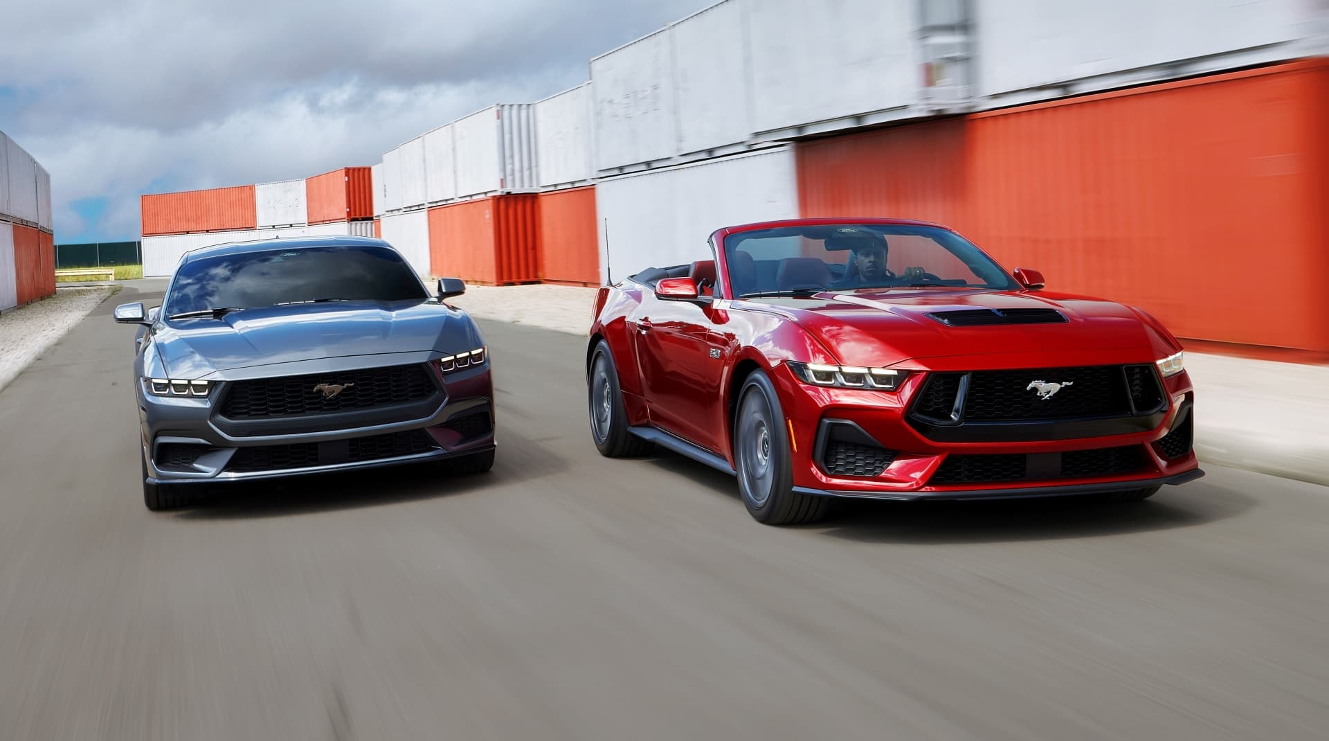 Dos Ford Mustang en paralelo, uno rojo y otro gris, ambos con diseño lateral imponente.