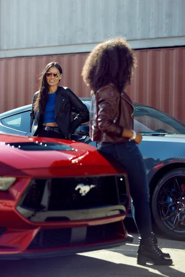 Dos mujeres conversando junto al frontal de un Ford Mustang, resaltando su agresivo diseño.
