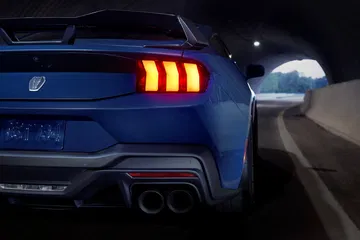 Vista trasera de un Ford Mustang iluminando la noche con sus distintivas luces traseras.