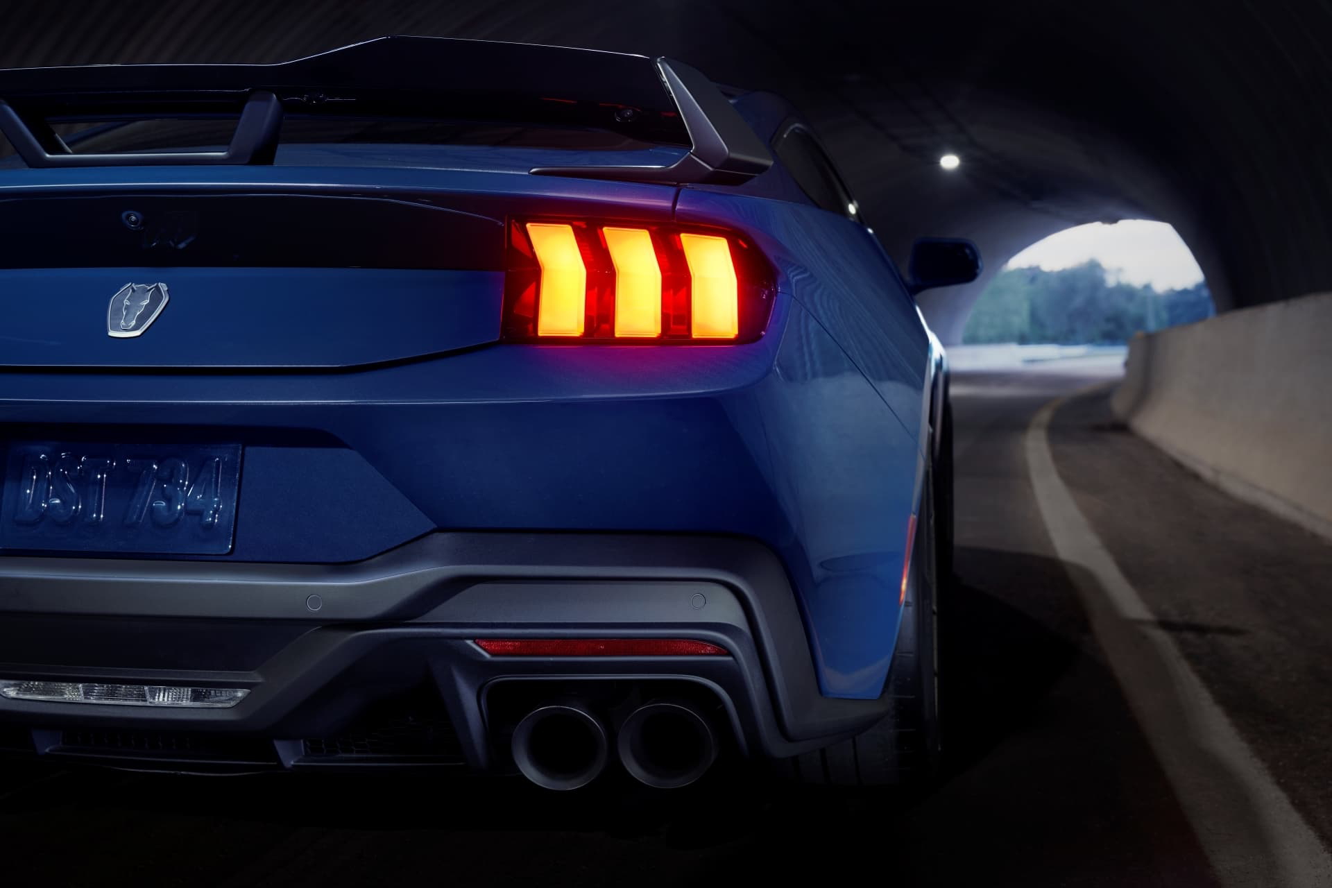 Vista trasera de un Ford Mustang iluminando la noche con sus distintivas luces traseras.