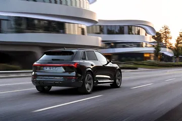 Vista dinámica de un Audi Q8 e-tron en entorno urbano, resaltando su diseño trasero y lateral.