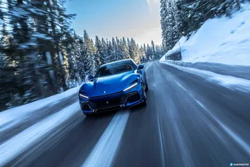 Ferrari Purosangue azul en carretera nevada, mostrando su diseño frontal y lateral.