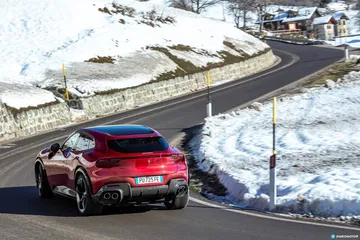 Vista dinámica del Ferrari Purosangue mostrando su trasera y perfil lateral en carretera nevada.