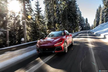 Ferrari Purosangue rojo recorriendo carretera nevada, vista frontal y lateral.