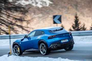 Vista lateral del Ferrari Purosangue sobre carretera nevada.