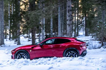 Vista lateral del Ferrari Purosangue rojo sobre un paisaje nevado.