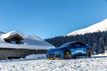 Vista lateral del Ferrari Purosangue sobre la nieve con montañas al fondo.
