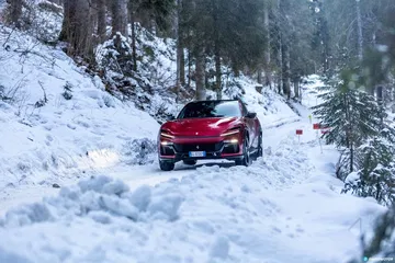 Vista lateral de un Ferrari Purosangue desafiando una carretera nevada.