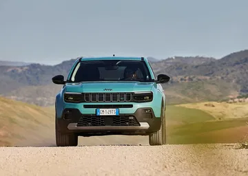 Vista frontal lateral del Jeep Avenger en terreno arenoso, mostrando su diseño robusto.