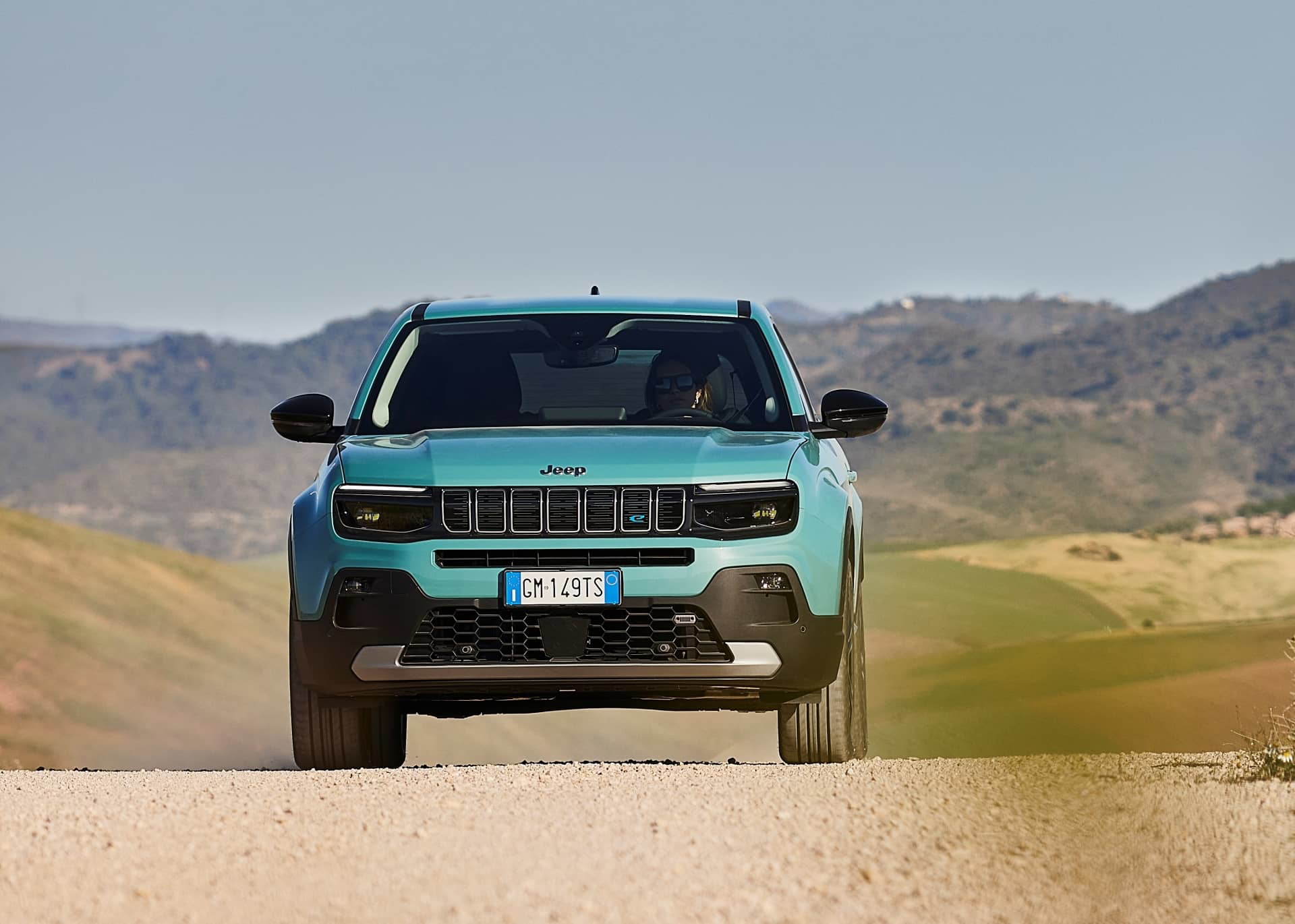 Vista frontal lateral del Jeep Avenger en terreno arenoso, mostrando su diseño robusto.