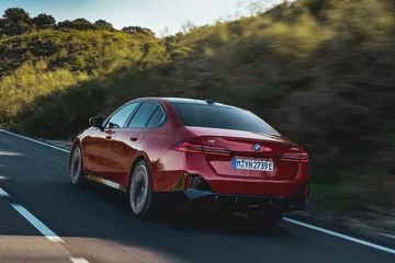 Vista dinámica de BMW Serie 5 en carretera, enfocando zona trasera y lateral.